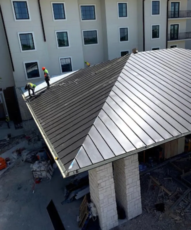 Crew installing standing seam metal roof panels on a commercial project in Hudson Falls
